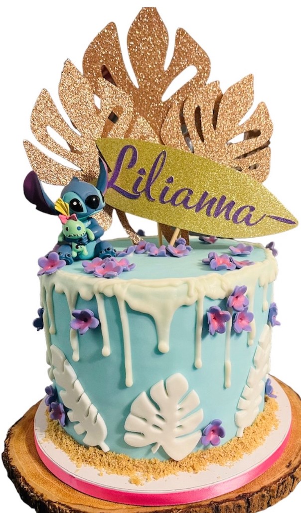 Tropical themed ice cream cake with turquoise frosting, white chocolate drip, and tropical flowers