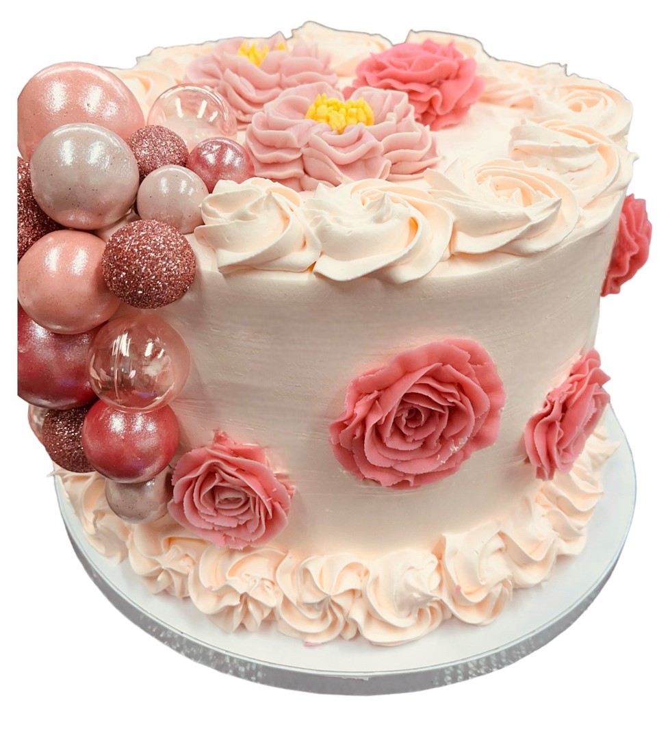 Light pink ice cream cake decorated with piped rosette flowers and pink metallic ornamental balls